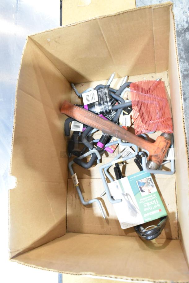 Cardboard box with assorted items including wires, tools, hooks, and a mesh bag. Items appear new with some product labels visible.