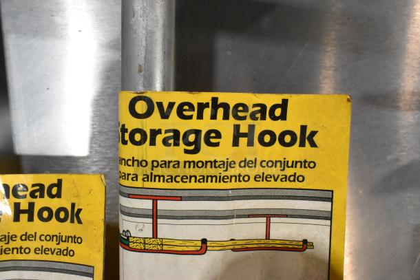 Overhead Storage Hook packaging, yellow label with illustration. Text in English and Spanish for elevated storage hook assembly.