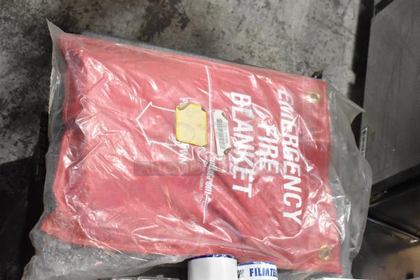 Red emergency fire blanket in sealed package with labels, stored in trunk. Appears in new condition.