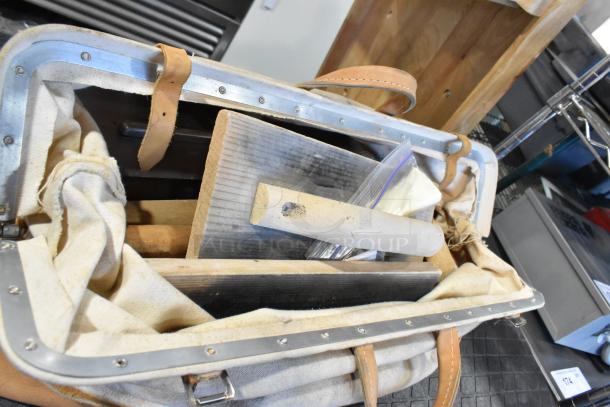 Two canvas bags with leather straps, containing various tools including trowels and wooden handles, in used condition.