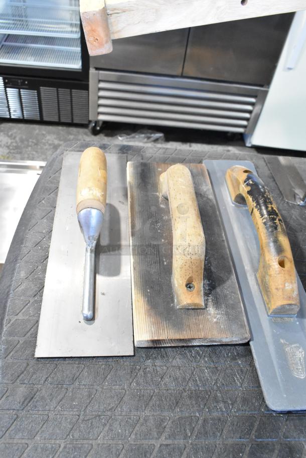 Various trowels with wooden handles on a textured surface; visible signs of use. Includes metal and wood finishes.