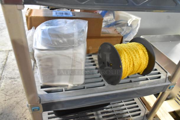 Auction lot with yellow rope on spool and sealed poly bins on a metal shelf. Includes boxes; mixed condition items.