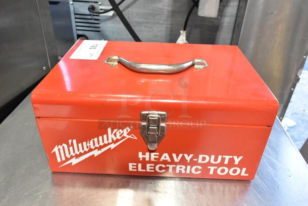 Milwaukee Electric Holeshooter in red metal tool box, sturdy handle, secure latch, brand logo, and "HEAVY-DUTY ELECTRIC TOOL" text.