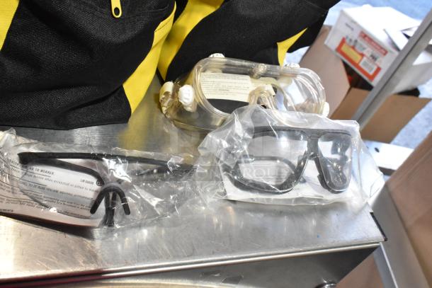 Three black and yellow bags with contents, including a dusting brush and kneepads. Safety goggles and glasses included.