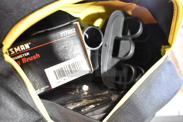 Three black and yellow bags with contents, including a dusting brush and kneepads, partial Craftsman box visible.