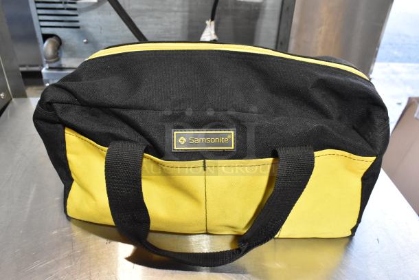 Black and yellow Samsonite bag with contents, including a dusting brush and kneepads. Features durable fabric and sturdy handles.
