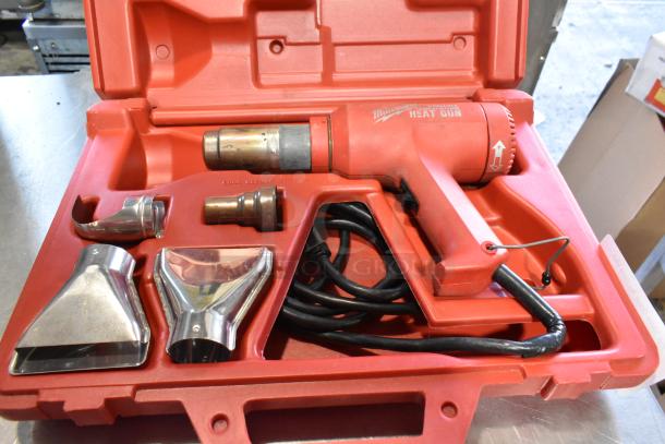 Milwaukee electric heat gun in red hard case, 120 volts, with three metal nozzles, cord, and marked controls.