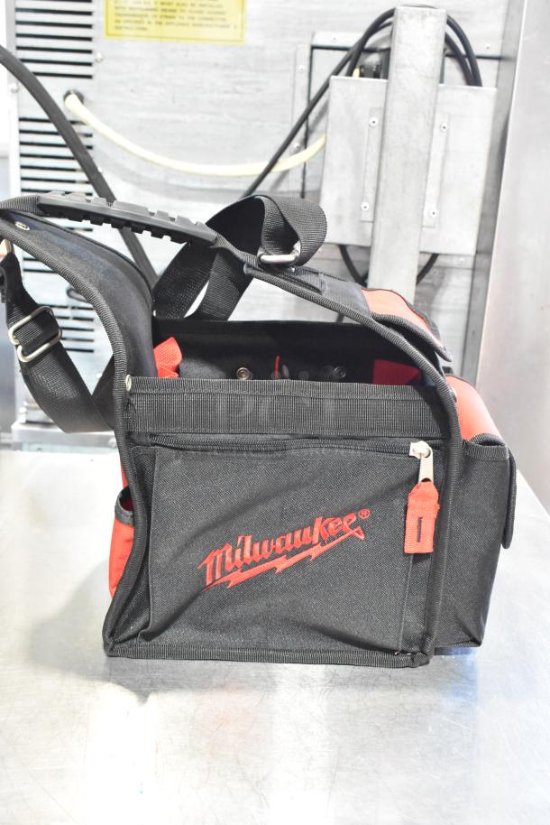Milwaukee soft tool bag with red logo, adjustable shoulder strap, multiple pockets, and durable black fabric.