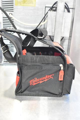 Milwaukee soft tool bag with red logo, adjustable shoulder strap, multiple pockets, and durable black fabric.