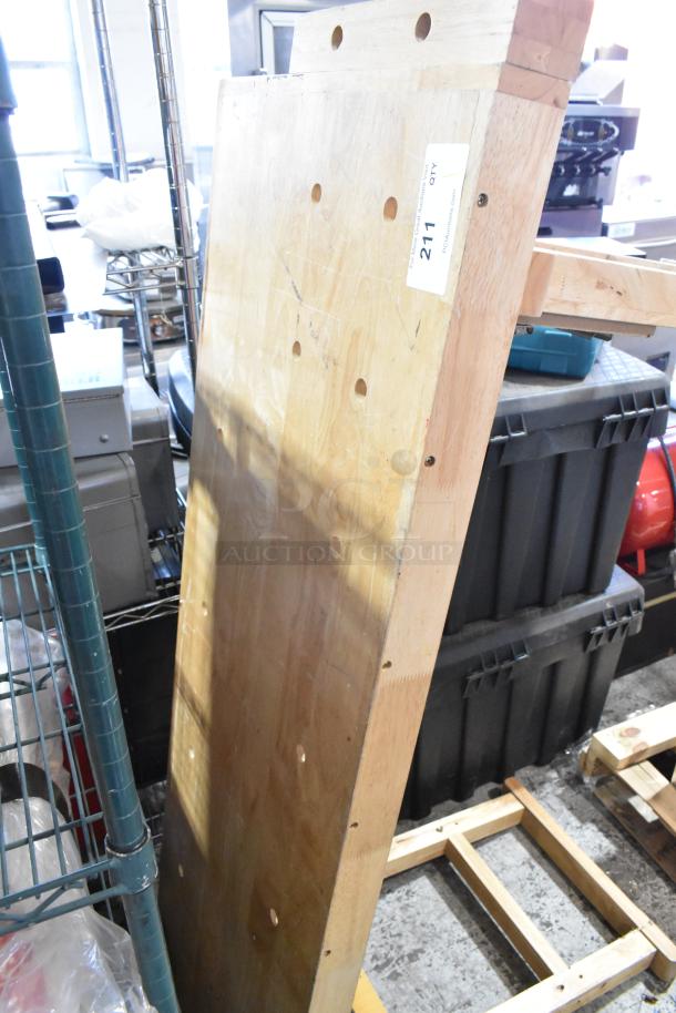 Wooden table with visible natural grain, flat surface, and drilled holes. Auction tag "211" attached. Good condition.