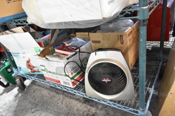 Tier lot with a Vornado fan, assorted books, and boxed items on a wheeled metal shelf. Various conditions.