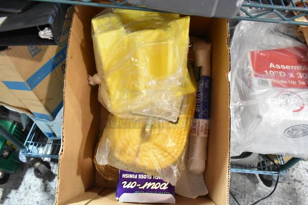 Box of assorted items including a caulk gun, binders, jumper cables, and packaging materials. Items appear used.
