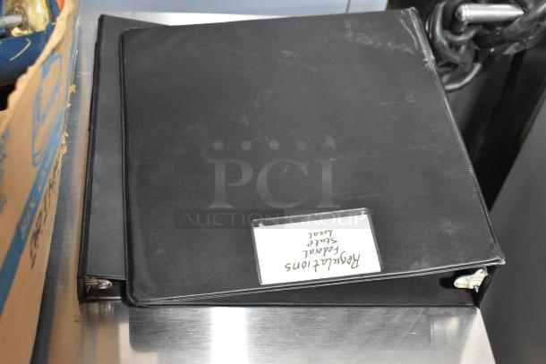 Alt text: Black binder on table, labeled "Redacted Federal Select Local," next to a cardboard box.