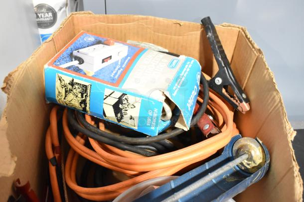 Box of assorted items including a caulk gun, jumper cables, and binders. Notable wear on the packaging, mixed condition.