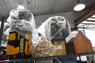 Alt text: Auction tier lot with a yellow tool bag, various plastic-wrapped items, plaid cloth, and a wooden box. Lot tag marked "216".