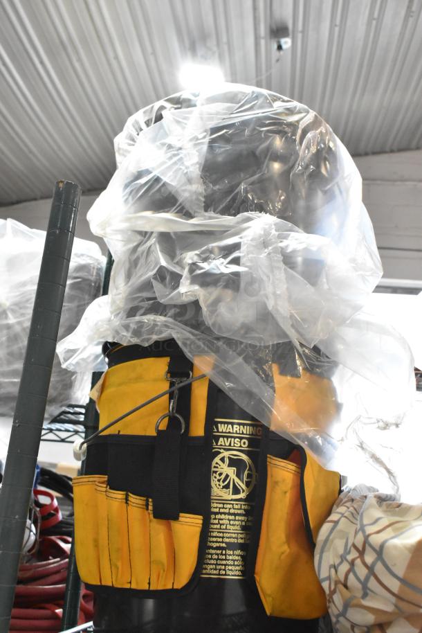 Yellow and black tool bag with multiple pockets, wrapped in plastic. Warning label visible, indicating safety instructions.