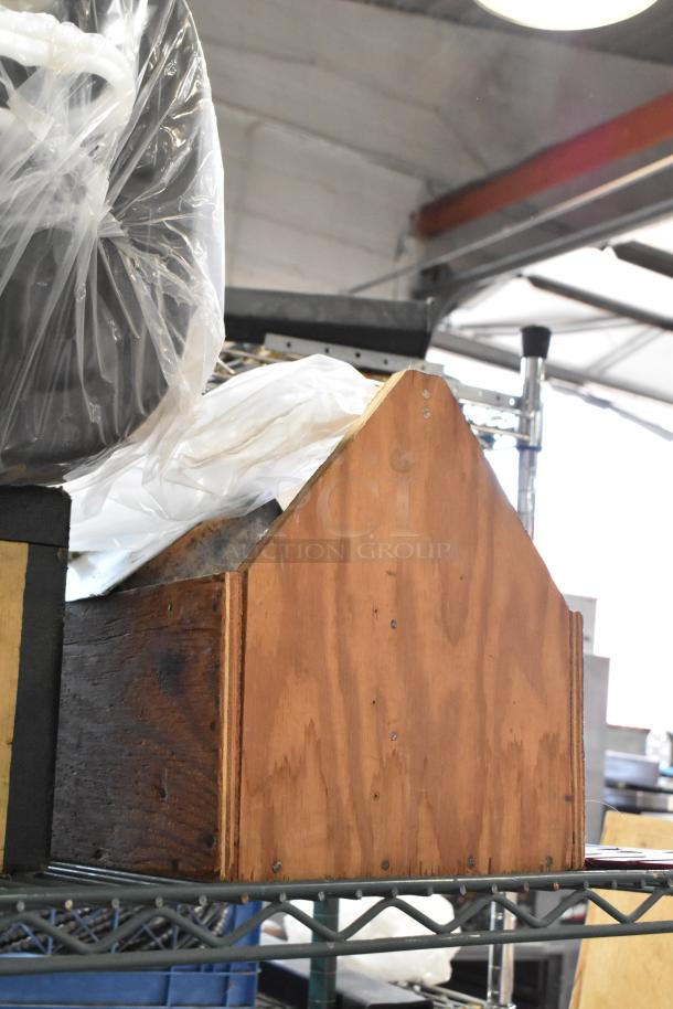 Tiered lot featuring various items including a wooden storage box, plastic-wrapped objects, and a tool bag, all on a metal shelf.