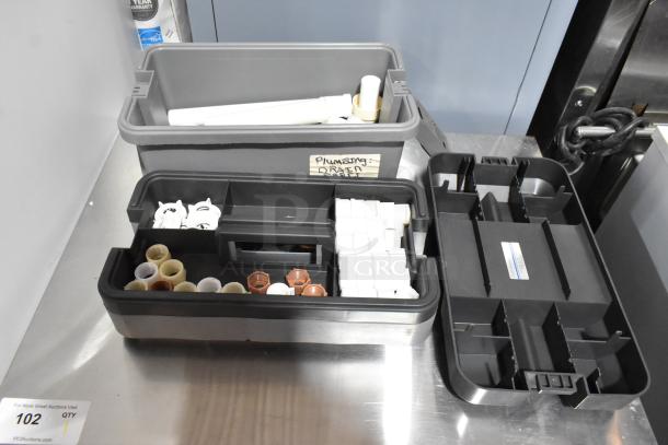 Three gray poly toolboxes containing plumbing components and connectors, labeled "Plumbing: Drains."