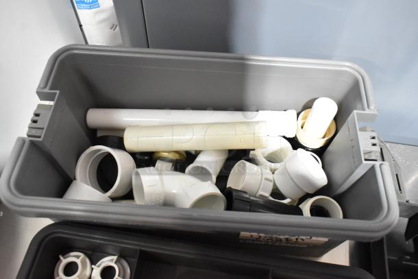 Three gray poly tool boxes containing assorted plumbing fittings, pipes, and connectors. Boxes show minor wear.