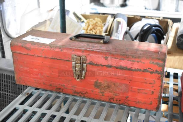Red metal tool box with visible rust and wear, containing tools. Includes a metal latch and a black handle. Auction lot 223.