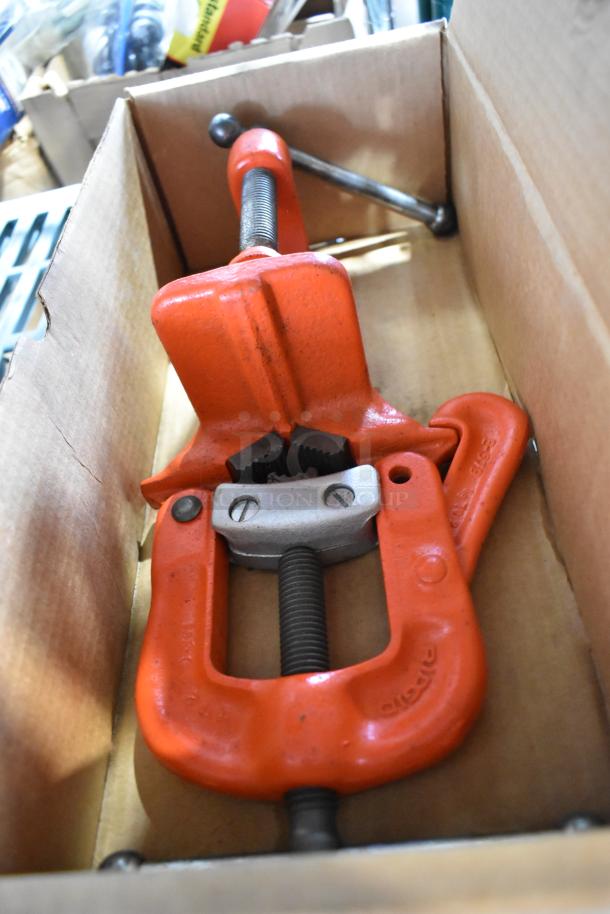 Red yoke vise in new condition inside a cardboard box, featuring a sturdy design with visible threading and clamp jaws.