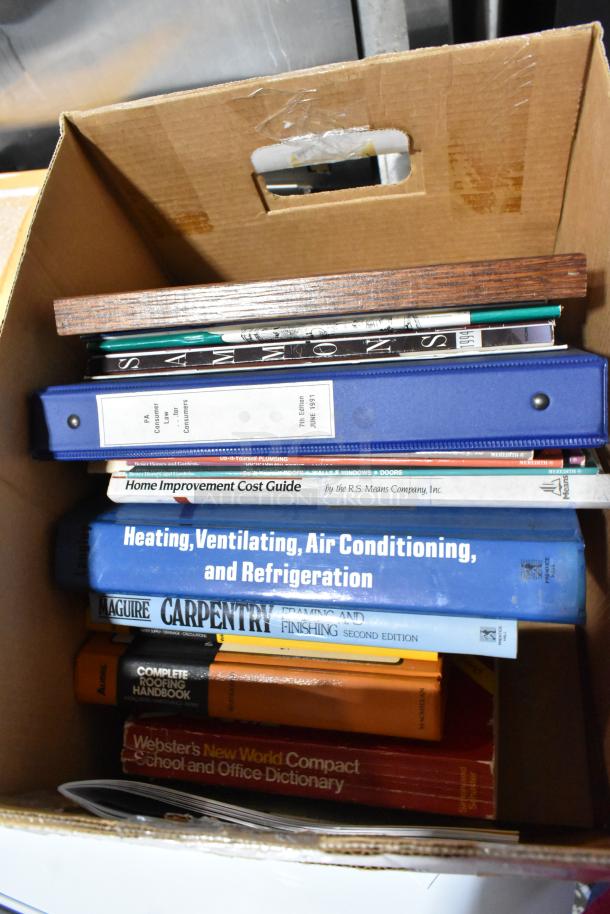 Cardboard box with assorted books and binders, including topics on home improvement, HVAC, carpentry, and dictionaries.