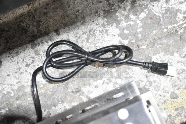 Power cord of the Vollrath TSI7021 Panini Grill resting on a concrete surface.