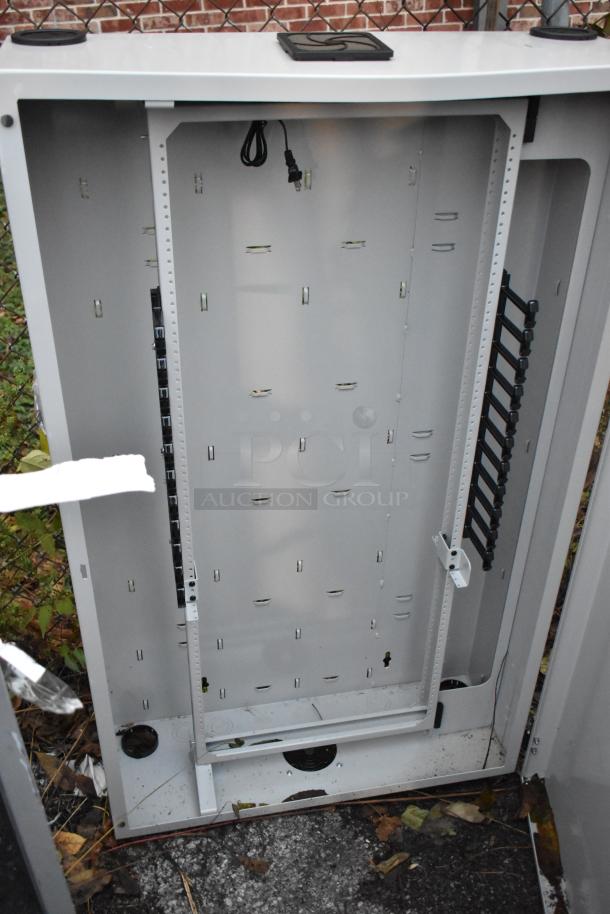 Legrand gray metal cabinet, open with multiple slots and a hanging power cord. Some signs of outdoor exposure visible.