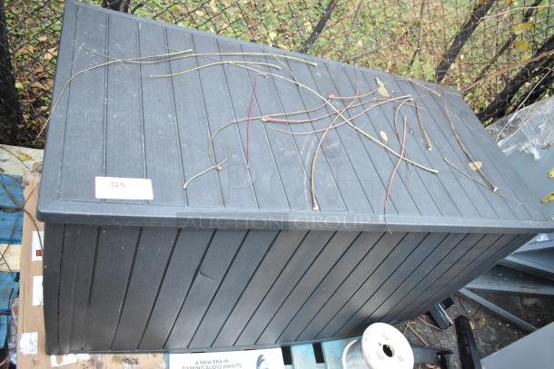 Deck storage box with lid, black, horizontal slats, tag labeled "325". Contains 16 umbrellas, exterior wear visible.