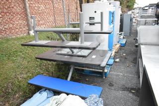 Outdoor dining table with attached benches, metal frame, stacked on pallets. Good condition, suitable for commercial use.