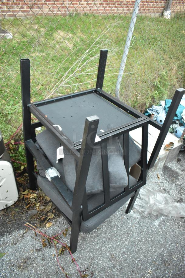 Set of two black metal chairs with cushions, stacked upside down. Appears in used condition, ideal for bidding.
