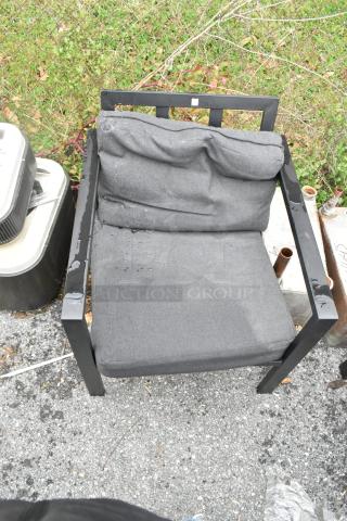 Black metal chair with grey cushions, showing signs of wear. Sturdy frame, outdoor setting. No visible tags or markings.