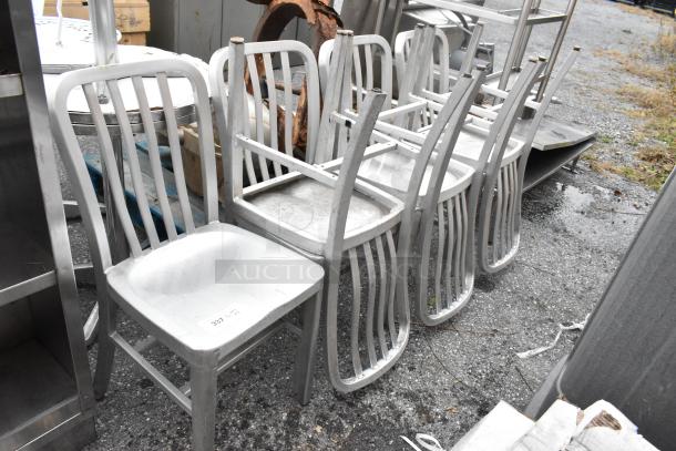 7 gray metal dining chairs, stackable, in used condition, suitable for indoor or outdoor use. Auction item tag visible.