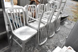 7 gray metal dining chairs, stackable, in used condition, suitable for indoor or outdoor use. Auction item tag visible.