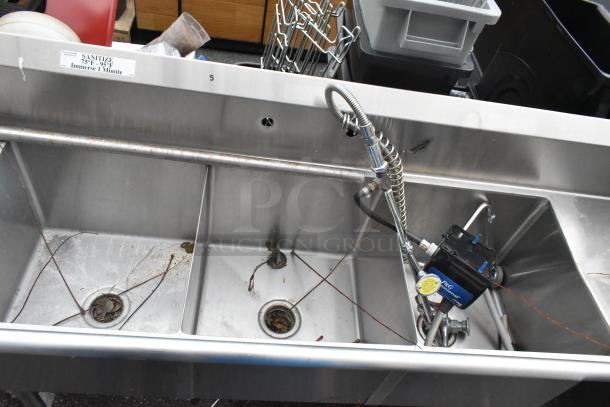 Stainless steel 3 bay sink with dual drain boards, integrated faucet, and sanitizer label. Visible wear marks.