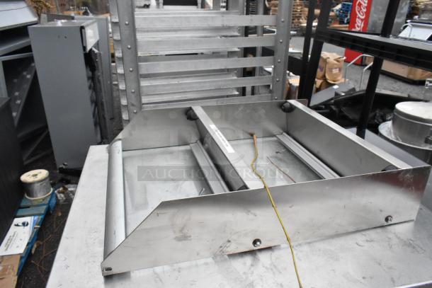 Stainless steel commercial counter with over shelf, showing signs of wear. Includes label marking for positioning.