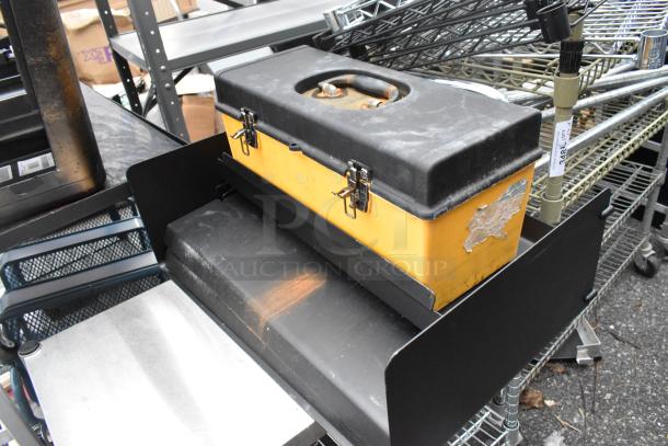 Wire 2-tier shelving unit on commercial casters with various contents, visible wear, and a yellow toolbox.