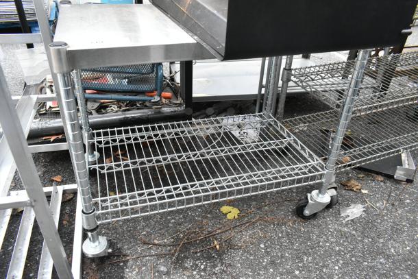 Wire 2-tier shelving unit on commercial casters, holds various tools and equipment. Sturdy metal construction, used condition.