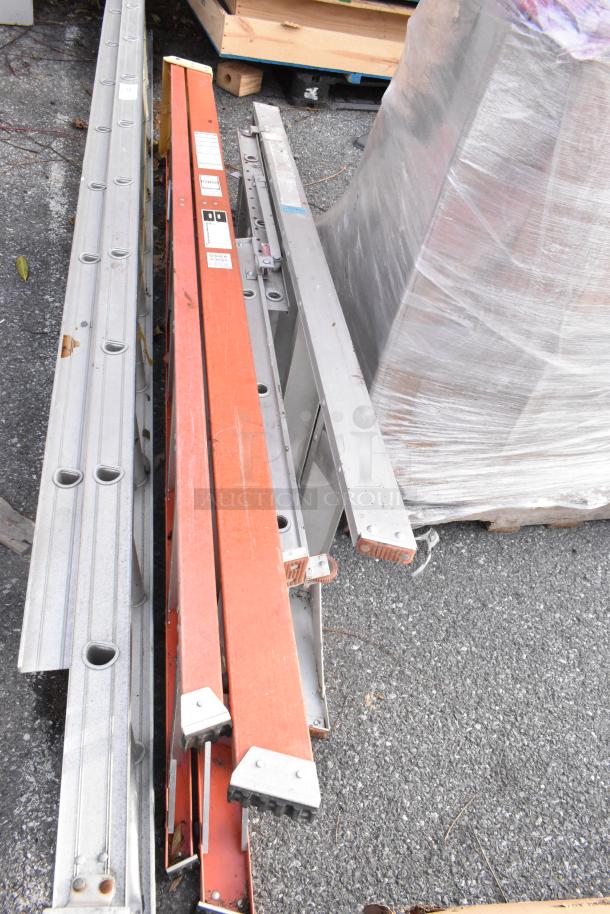 Three metal ladders, various styles, resting on the ground. Labels indicate model numbers. Some wear visible.