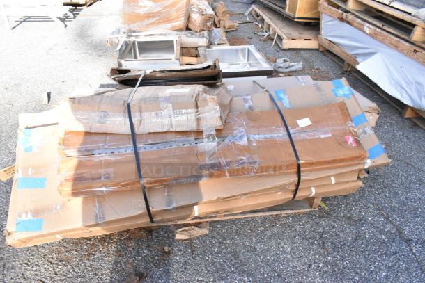 Stack of boxed "scratch and dent" items including Regency stainless steel shelves and Cambro serving trays. Boxes slightly damaged.