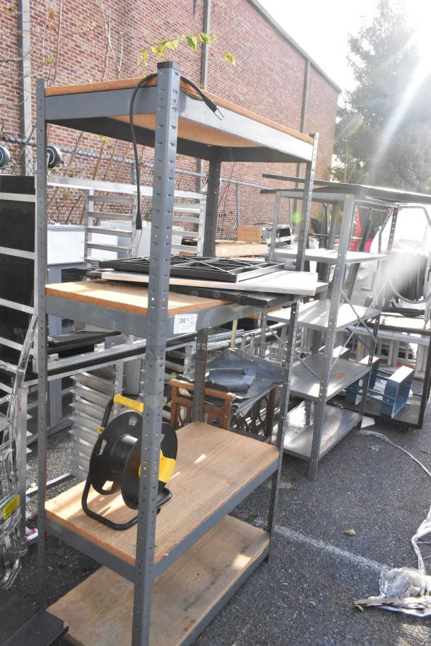 Three gray metal shelving units and a wooden 2-tier cart on casters. Good condition, industrial use. Auction tag visible.