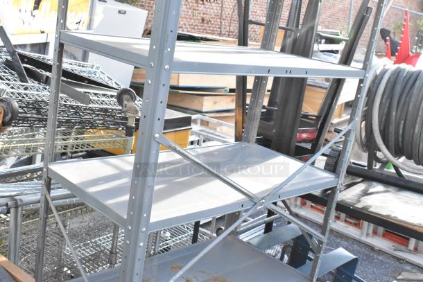 Gray metal shelving unit with sturdy frame, three tiers, and visible casters. Additional shelving items stacked. Good condition.