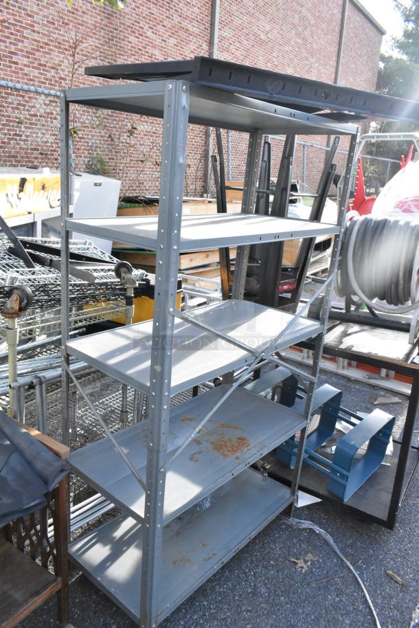 Gray metal shelving unit with multiple shelves, visible rust spots, and sturdy frame; part of a three-item auction set.