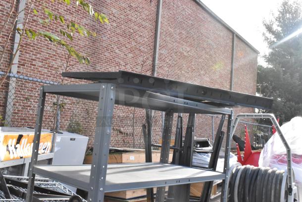 Gray metal shelving unit in good condition with three tiers, shown outdoors next to various other items.