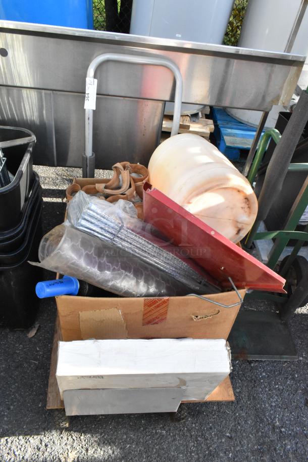 Flat cart loaded with mixed contents including a plastic drum, metal racks, rolls of material, and cardboard boxes. Item tag visible.