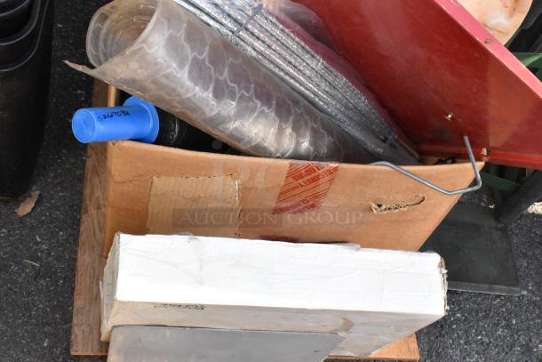 Flat cart carrying assorted items, including cardboard boxes, a blue handle, metal rods, and plastic wrap. Some boxes show wear.