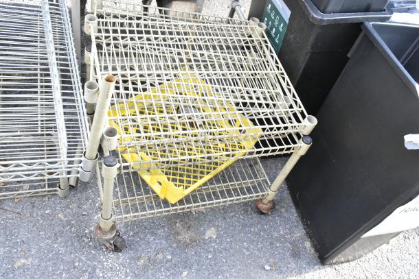 Three items including a wire shelving unit and a wire dunnage rack on wheels, fair condition, outdoor setting.