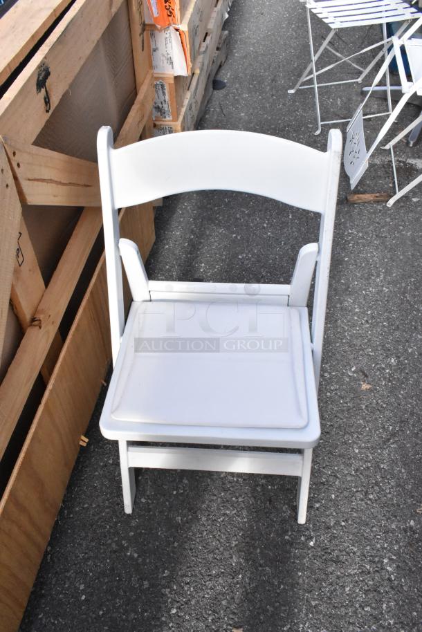 White folding chair on pavement; part of a lot of 56 chairs, white and black, in good condition for auction.