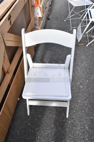 White folding chair on pavement; part of a lot of 56 chairs, white and black, in good condition for auction.