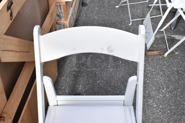 White folding chair, wooden frame, minimal wear. Part of a set of 56 white and black chairs. Suitable for events or gatherings.
